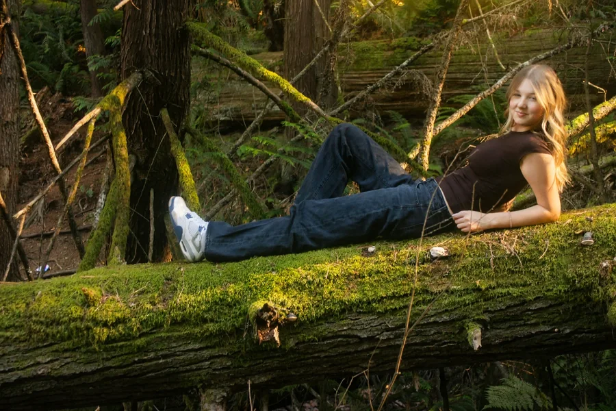 Lynden smiling while seated on a mossy log in the forest