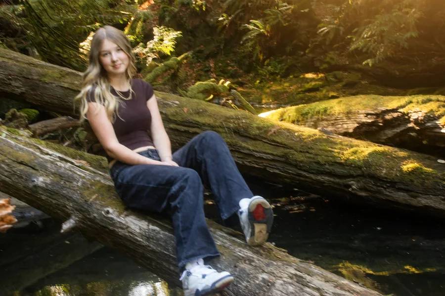 Lynden seated on a fallen log above the water in warm forest light
