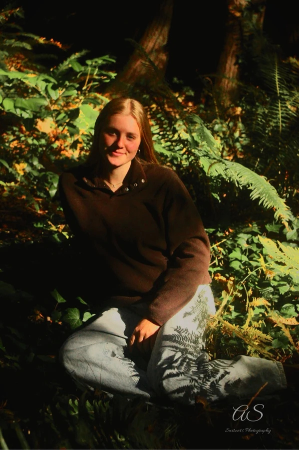 Young woman sitting among sunlit ferns in the forest