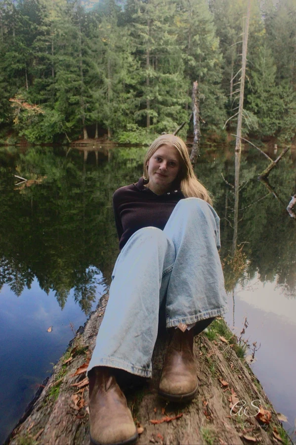 Young woman sitting on a fallen log above a still lake