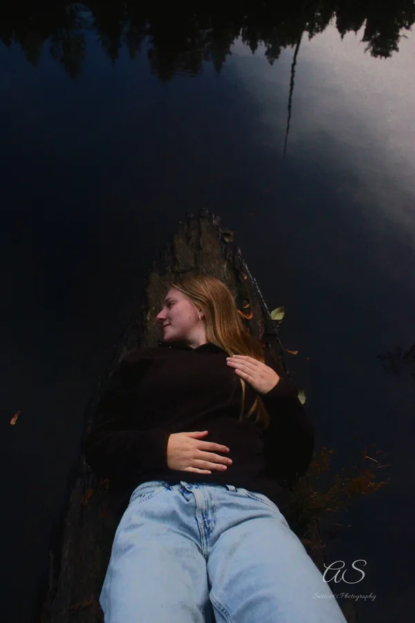 Young woman reclining on a log over dark reflective water