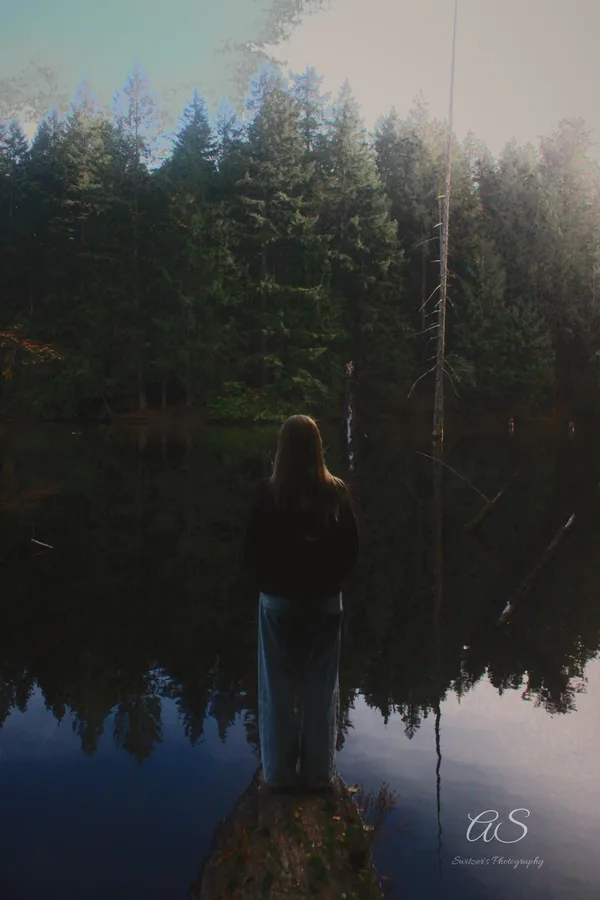 Silhouetted figure standing on a log above a mirror-calm lake