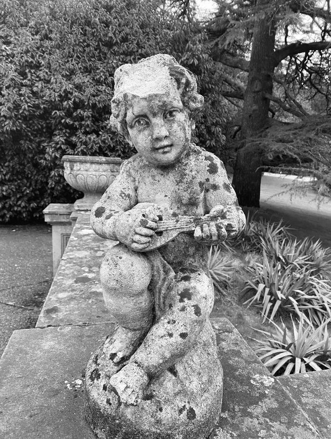 Black-and-white photograph of a weathered cherub statue holding an instrument