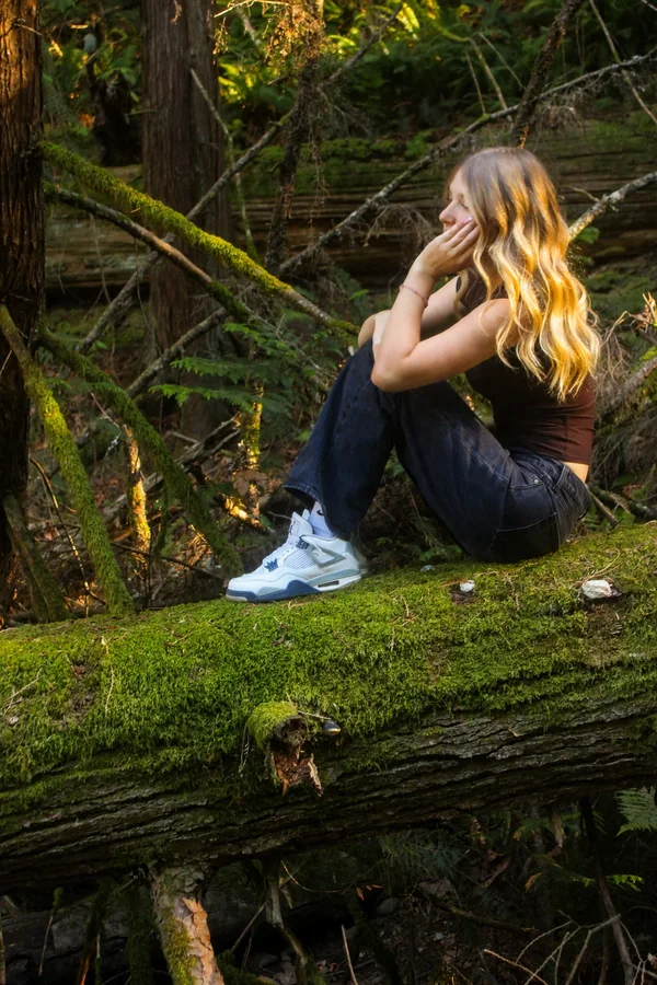 Lynden seated on a mossy log with a quiet gaze in the forest